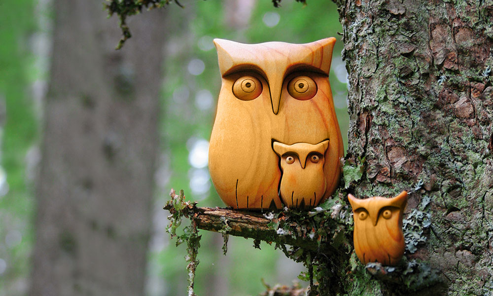 Waldfabrik Mama-Holzeule mit 2 Kindern sitzt auf einem Ast im Wald.